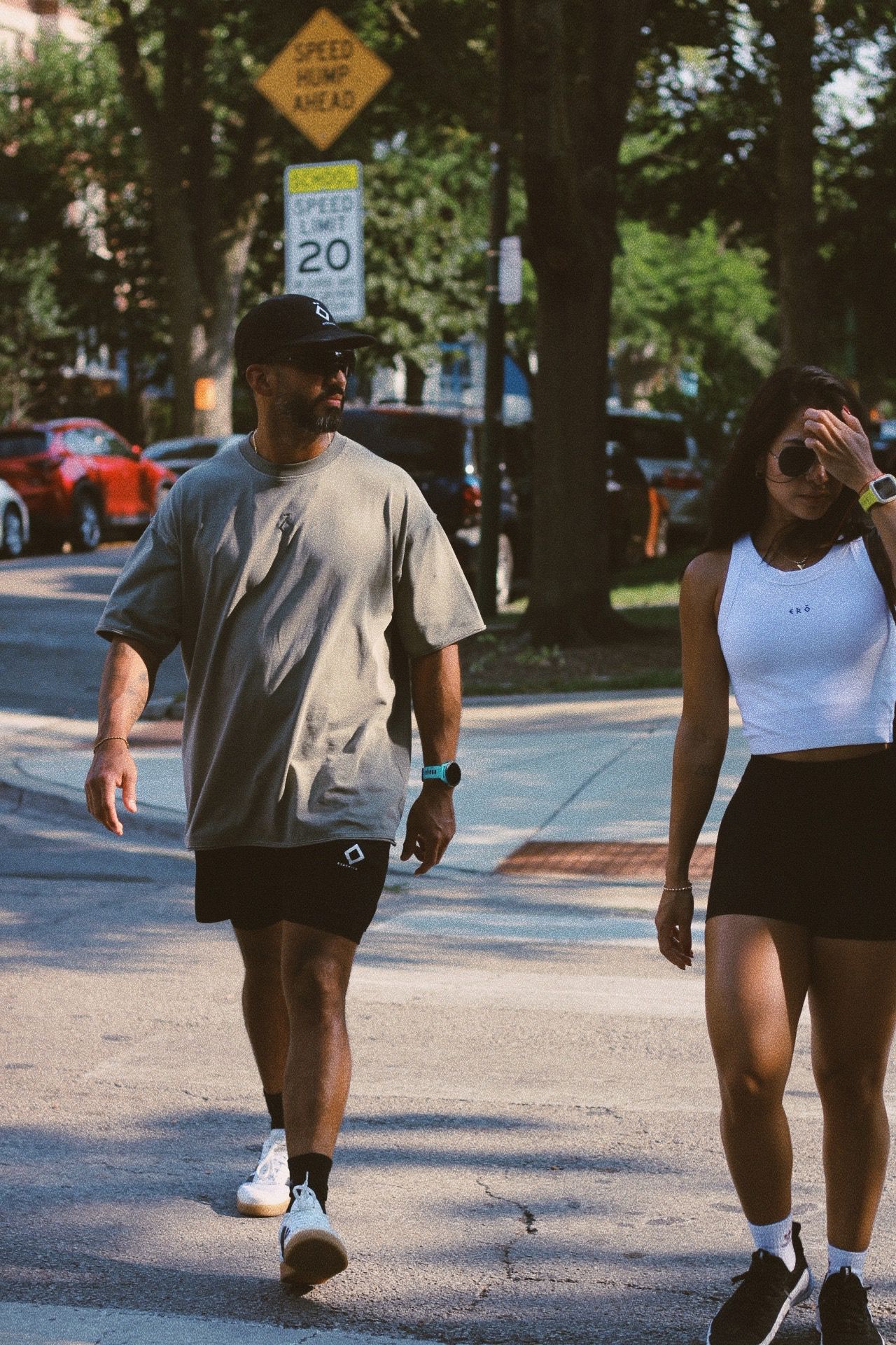 Two people walking on a street with trees and cars in the background