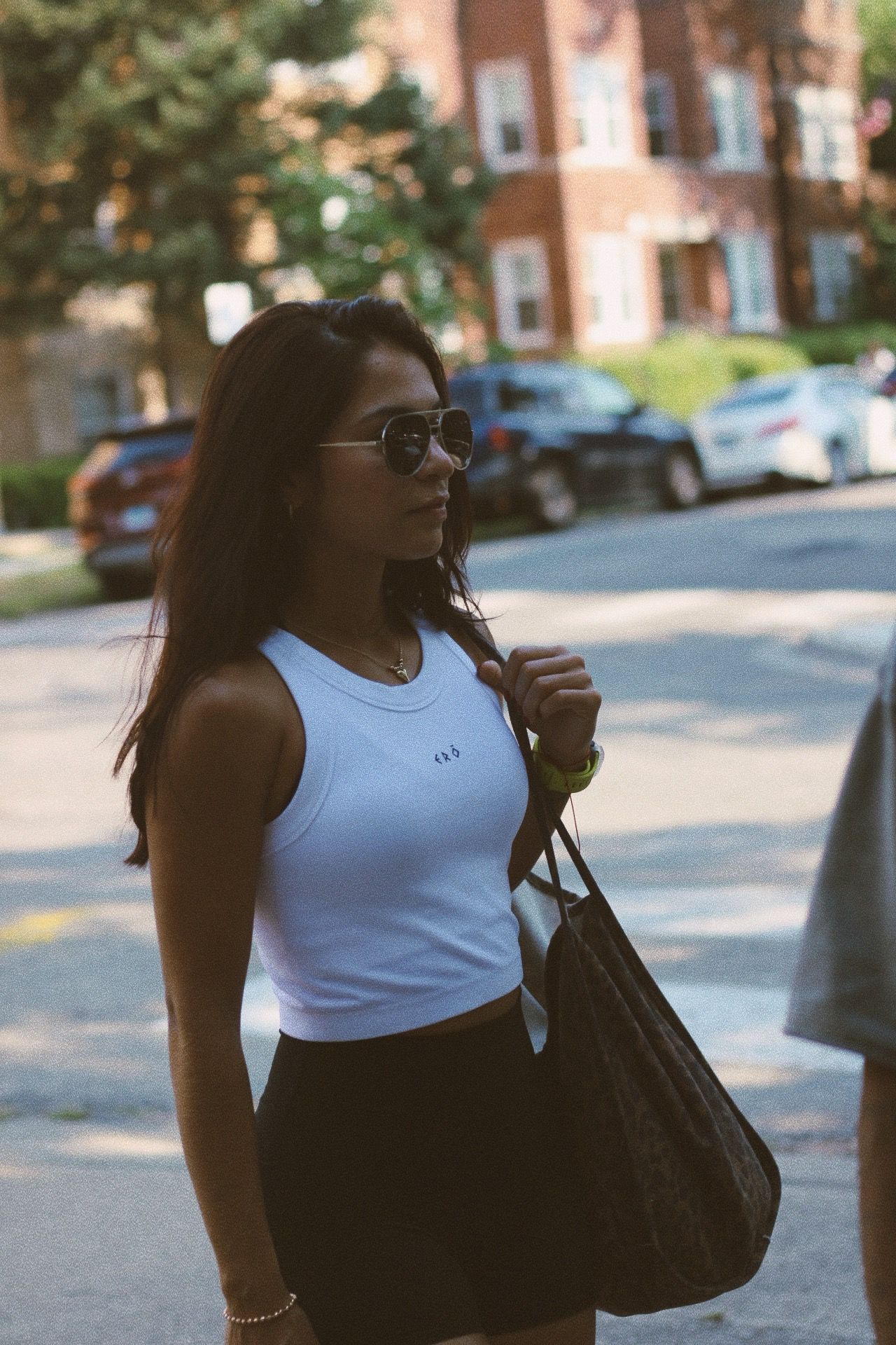 Woman in a white tank top and black skirt standing on a street with buildings in the background