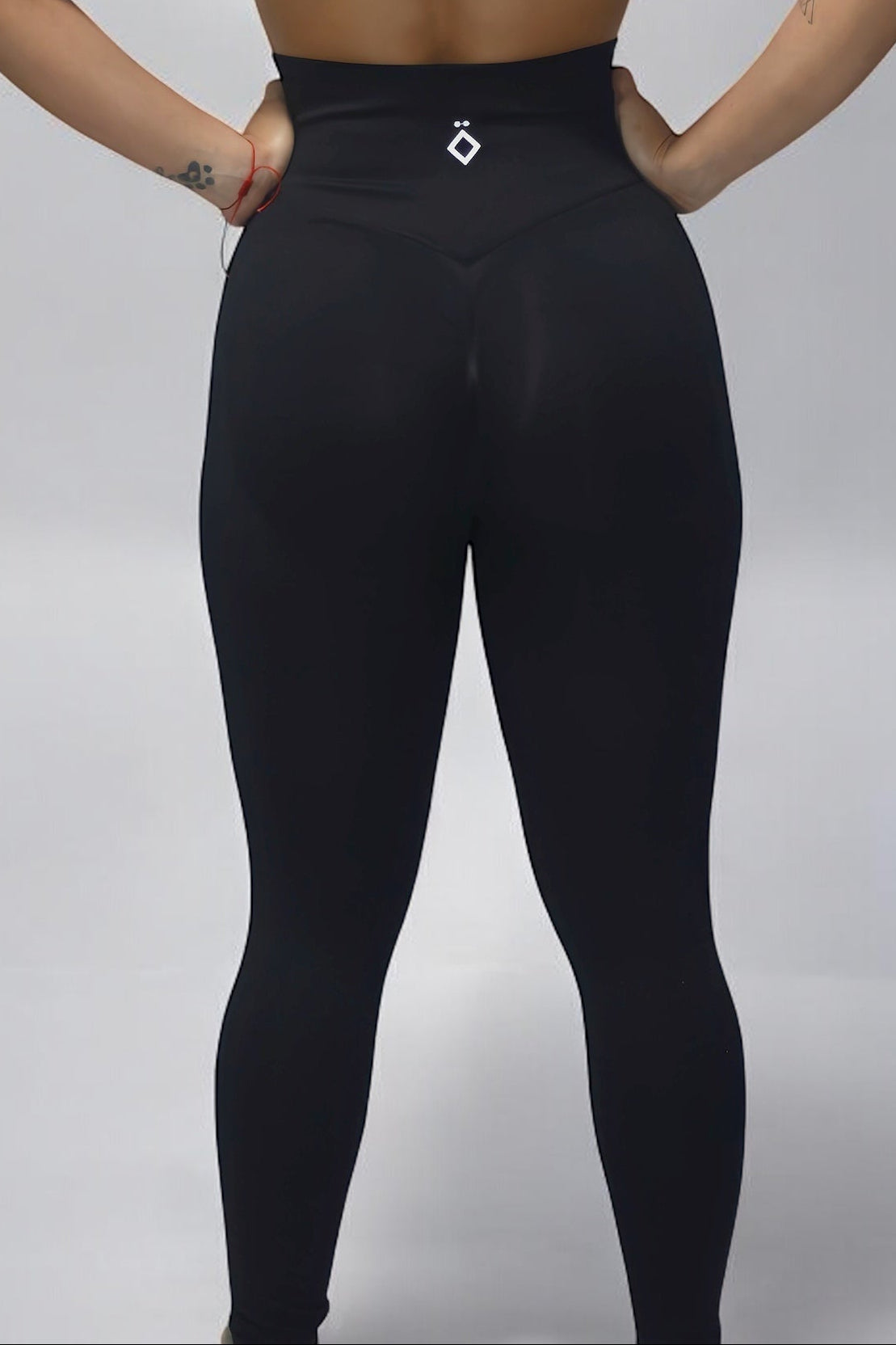 Person wearing a black strappy top and high-waisted pants on a plain background