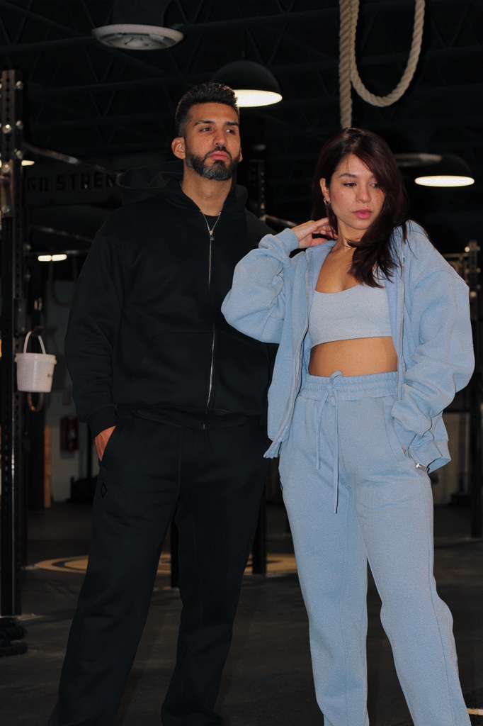 Two people, one in black and the other in a light blue tracksuit, standing indoors.